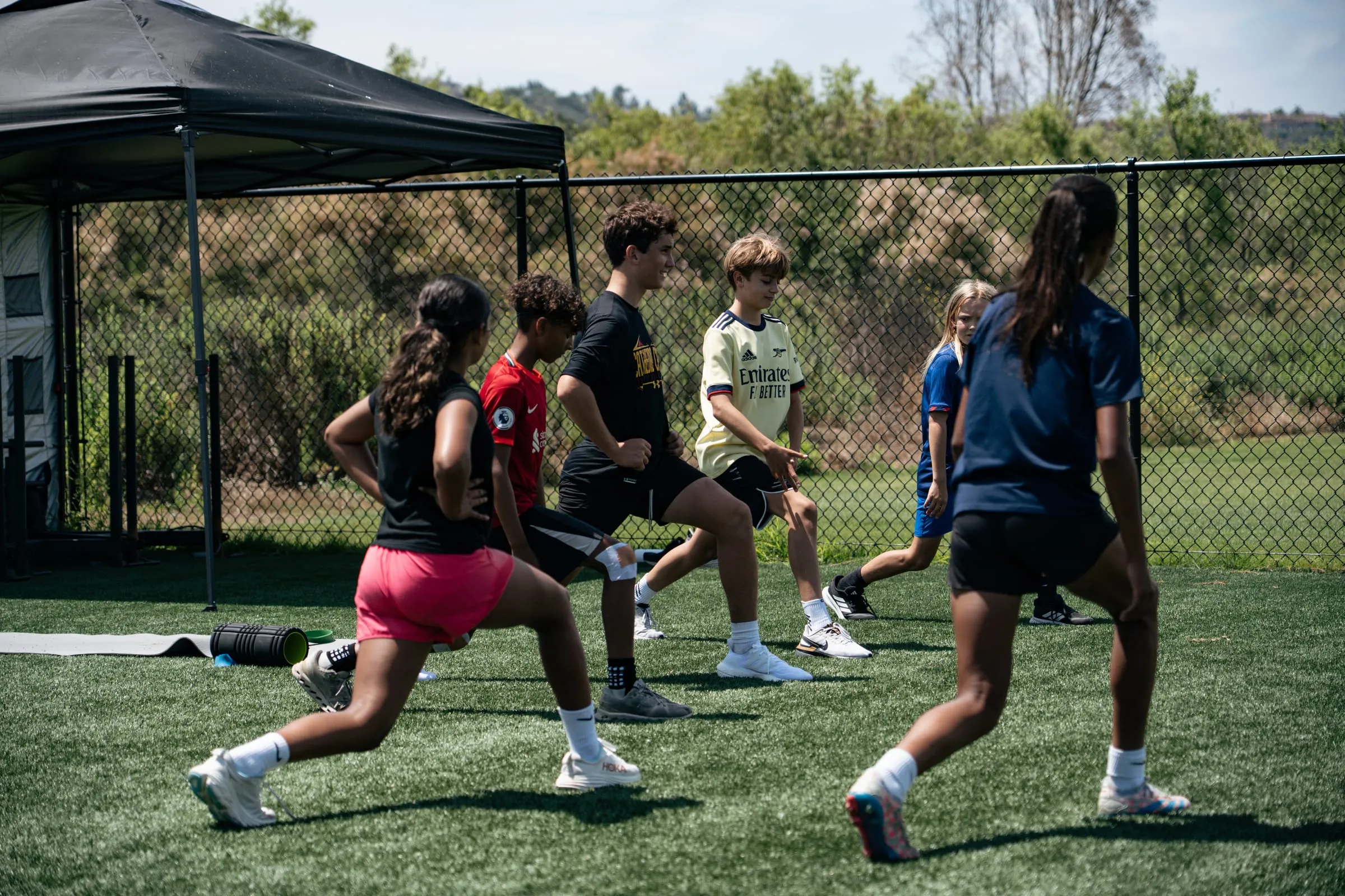 Young athletes doing walking lunges together on turf